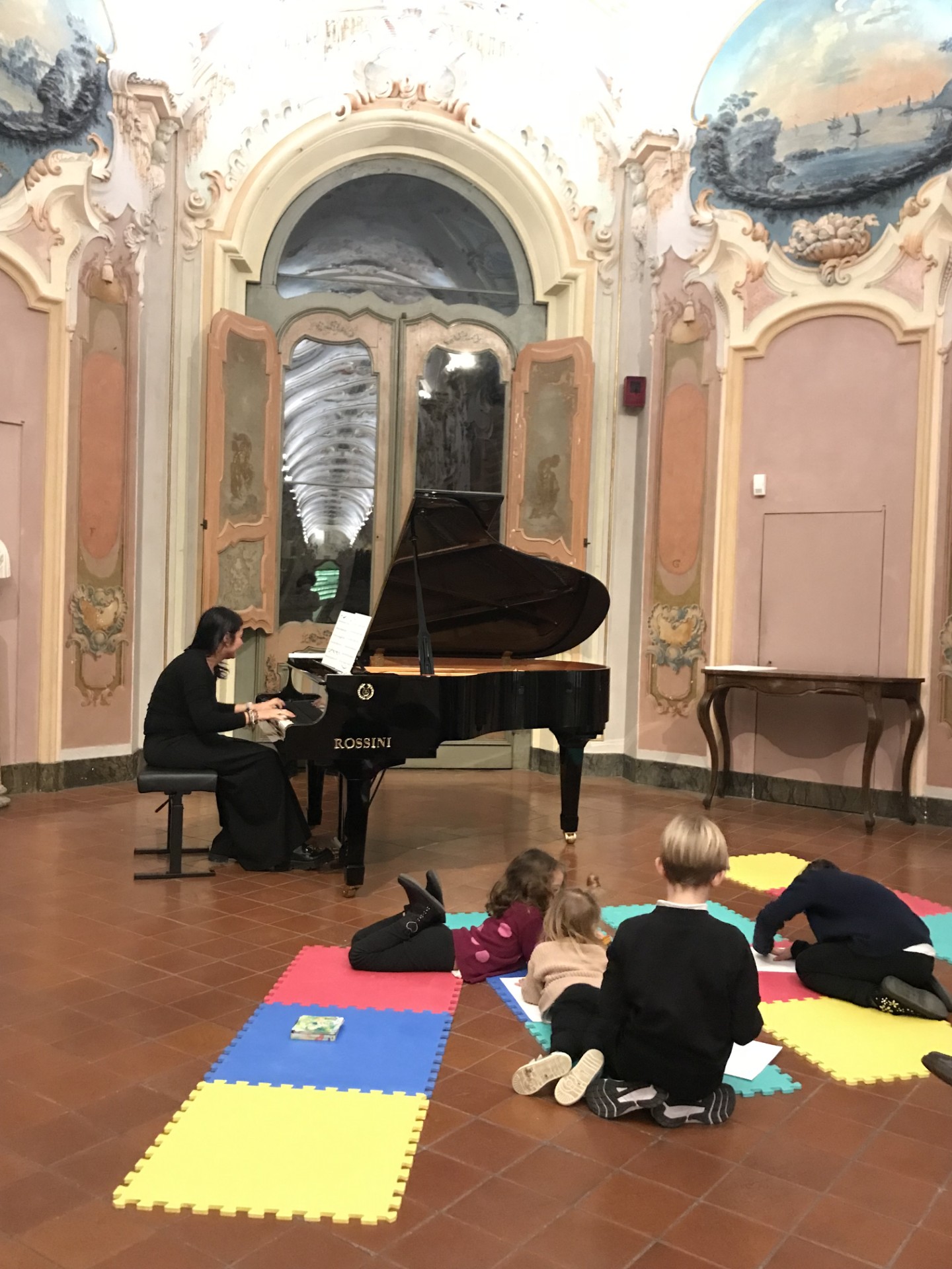 Bambini seduti a terra intorno a un pianoforte a coda